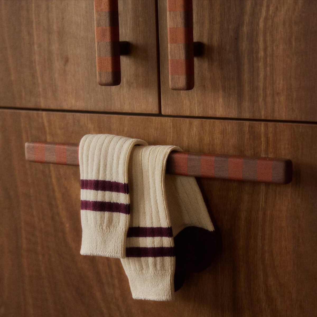 MILWORKS The Racquet Club Collection ribbed cotton socks in cream with burgundy stripes hanging on a wooden handle.