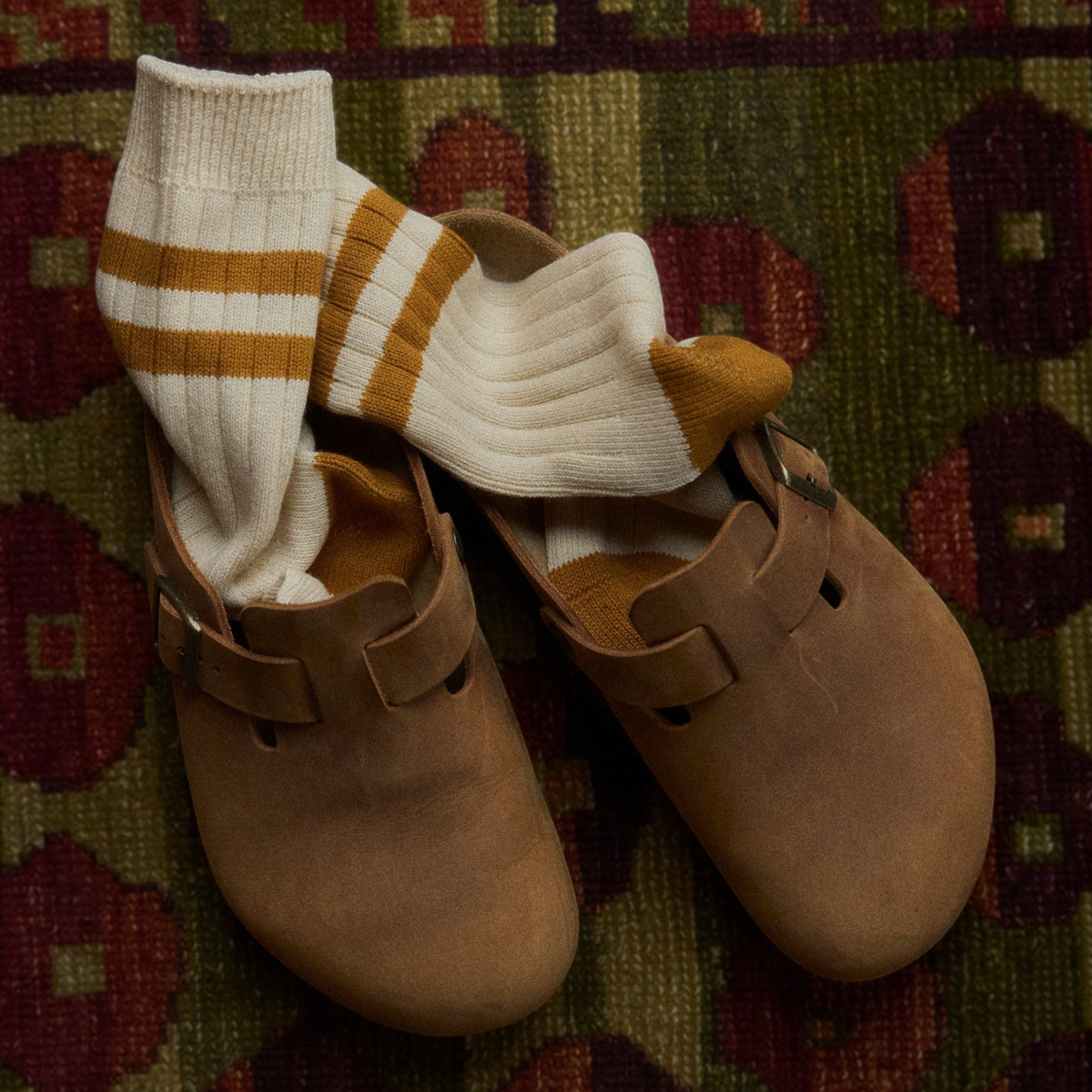 MILWORKS The Racquet Club Collection mustard and cream striped cotton socks tucked into brown suede clogs on a rug.