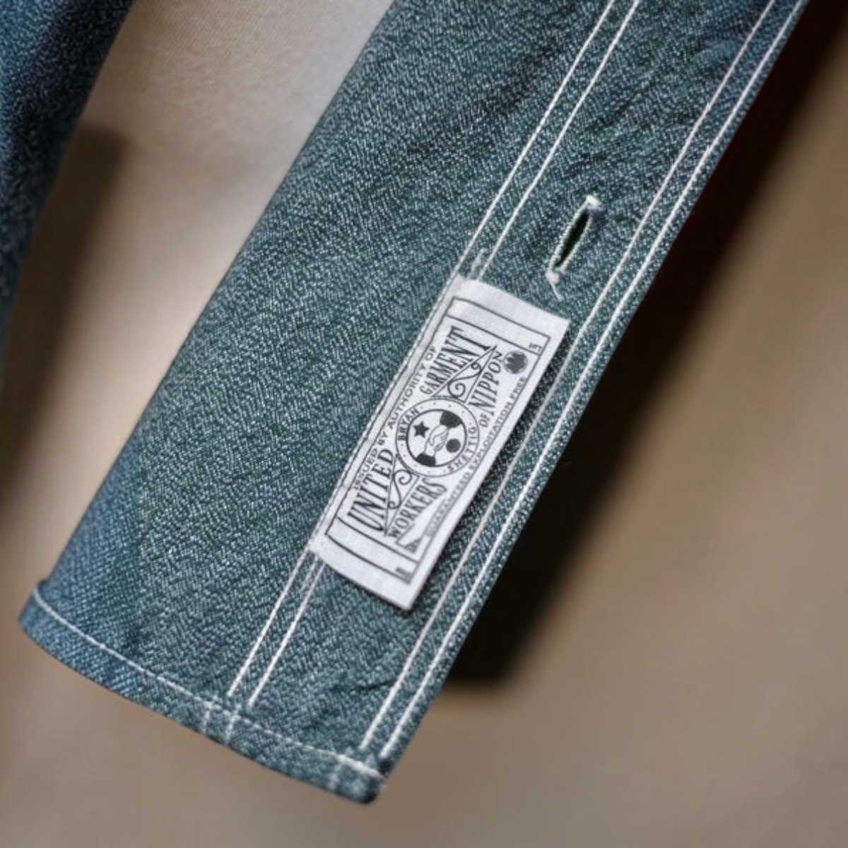 MILWORKS Atlas work shirt cuff in sage green salt and pepper selvedge chambray with a vintage-style garment worker tag.