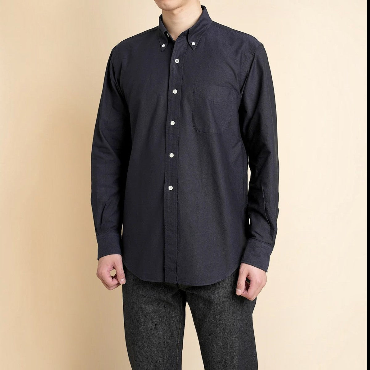 Kamakura navy cotton oxford button-down shirt with chest pocket and shell buttons worn by a man on a beige background.