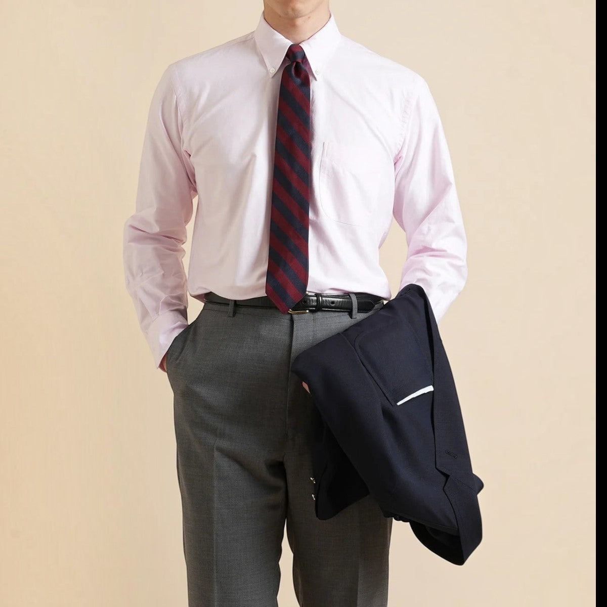 Kamakura pink cotton oxford button-down shirt with a striped tie, grey trousers, and a navy blazer over the arm.