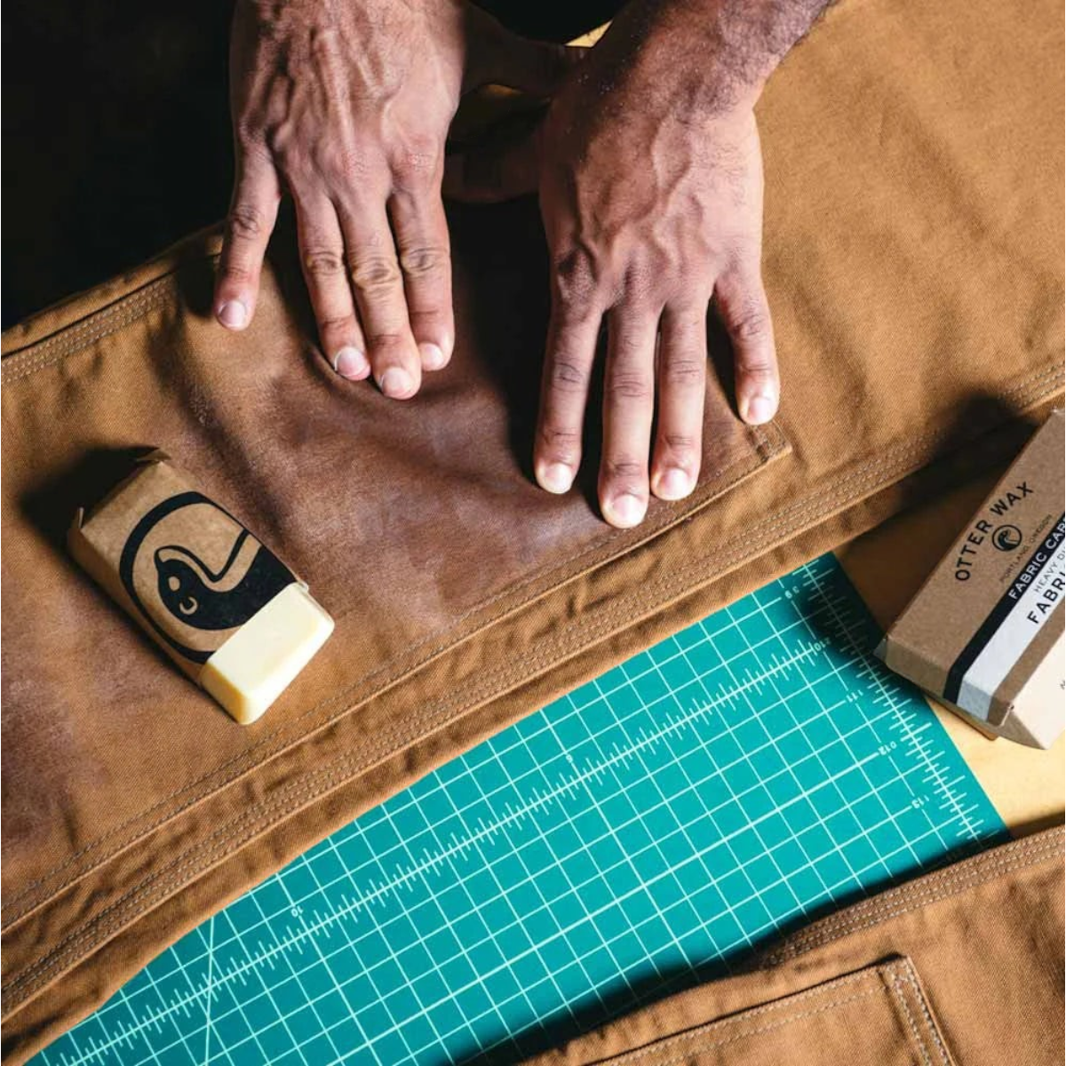 MILWORKS Otter Wax heavy duty fabric wax bar being applied to brown canvas fabric on a green cutting mat