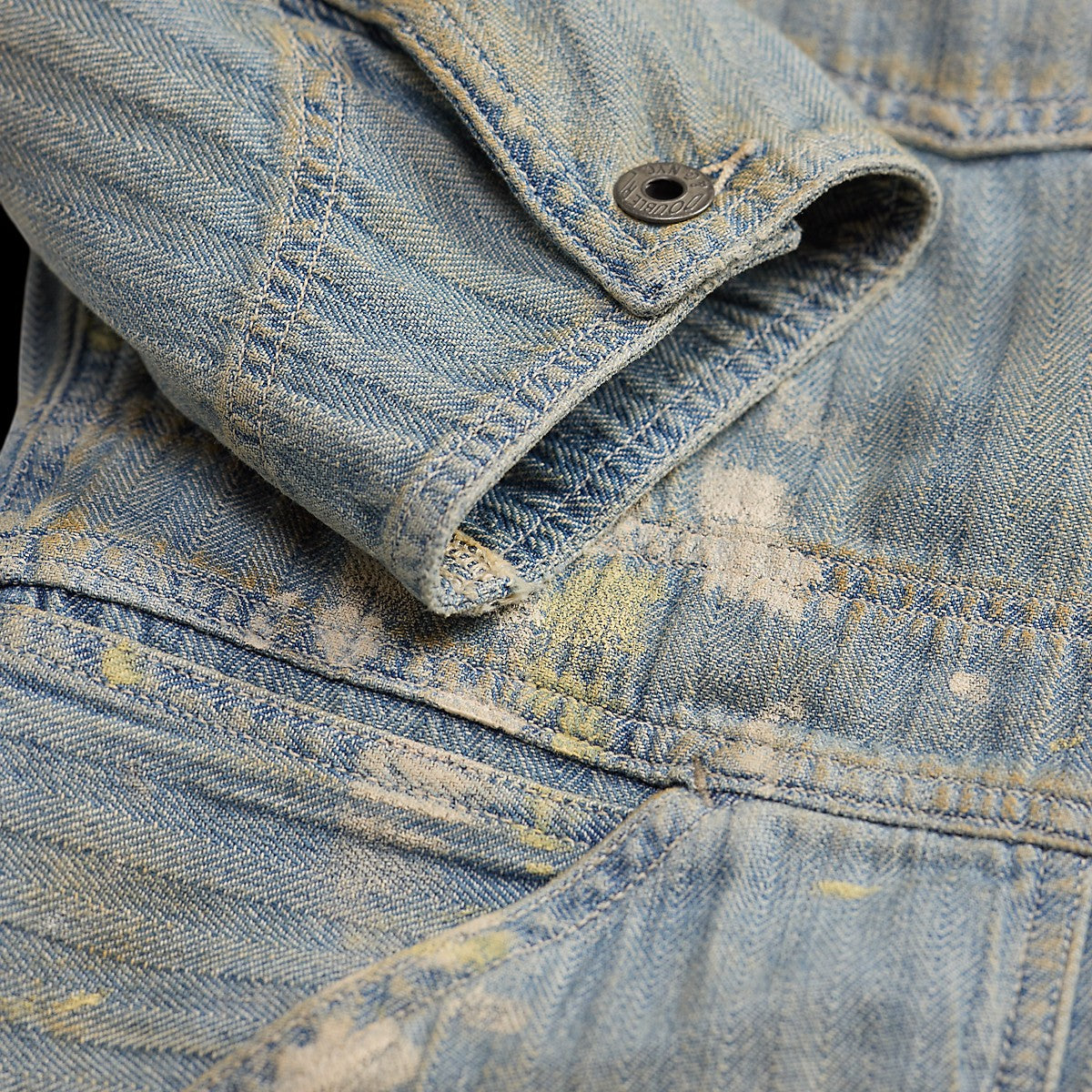 RRL distressed indigo herringbone cotton coverall sleeve detail with paint splatters and metal button