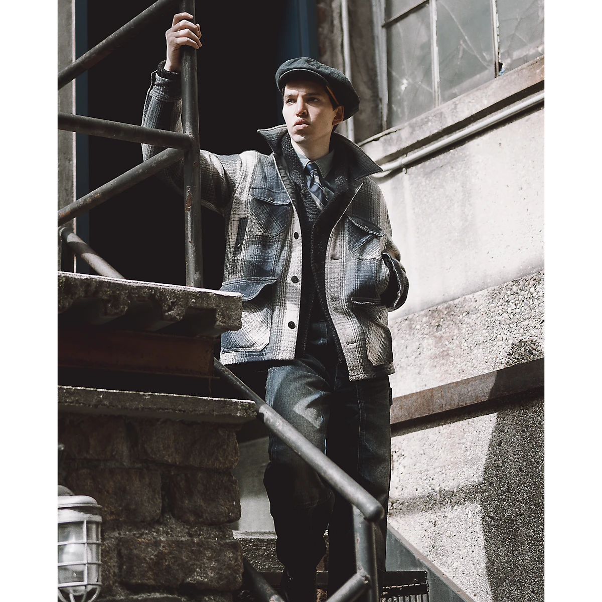 A man wearing a RRL blue and cream plaid wool twill overshirt with multiple pockets on an outdoor staircase.