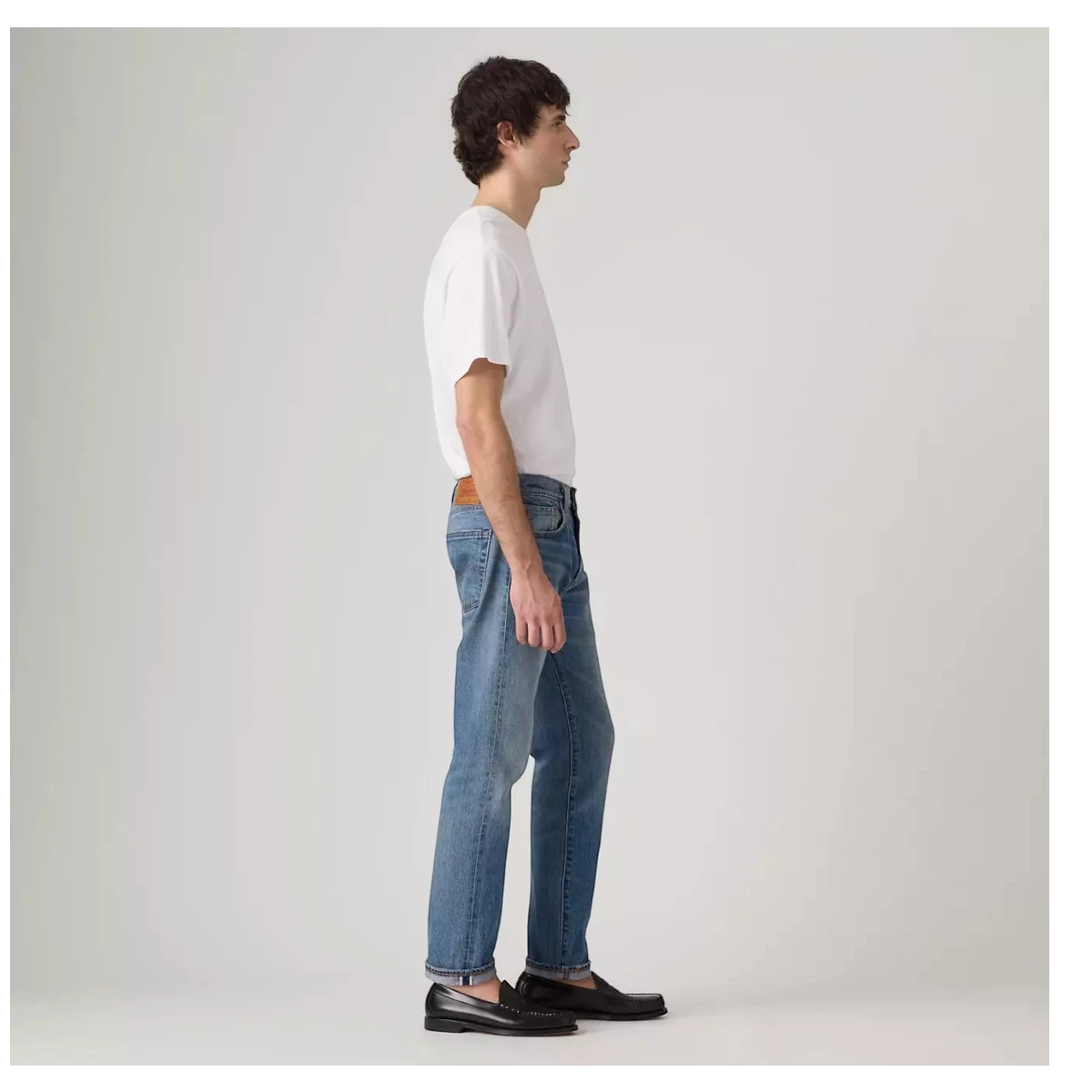 MILWORKS model wearing medium wash 502 Taper selvedge denim jeans with a cuffed hem and white t-shirt, side profile.
