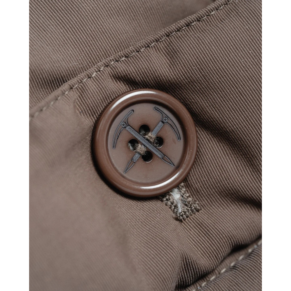 Close-up of a MILWORKS Arctic Parka in cappuccino brown featuring a custom button with an ice axe design.