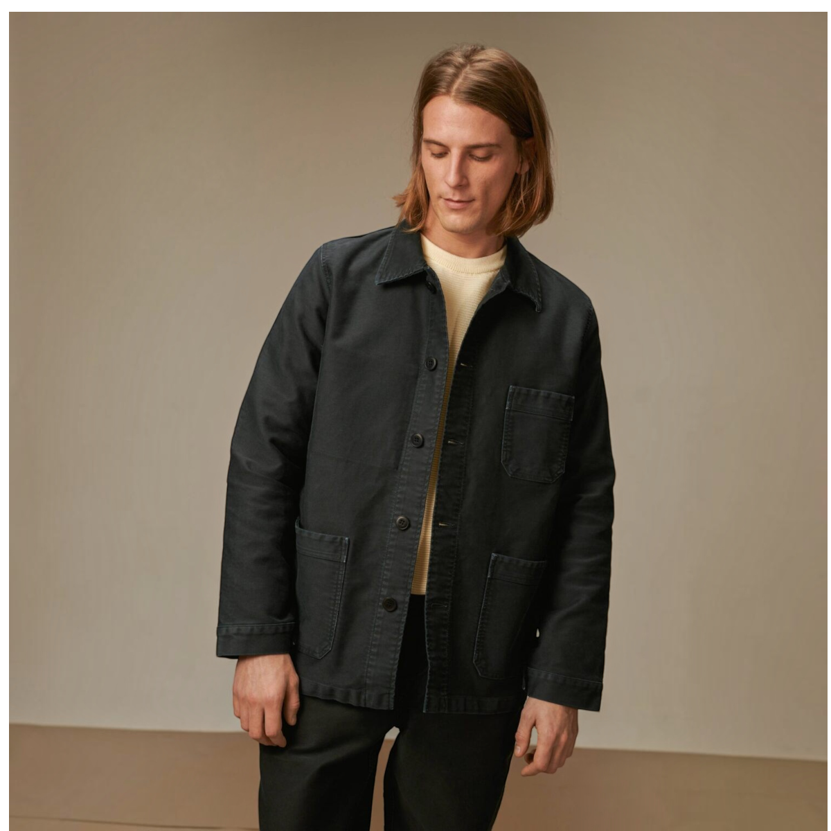 MILWORKS vintage washed black moleskin work jacket worn by a man with long hair over a cream sweater