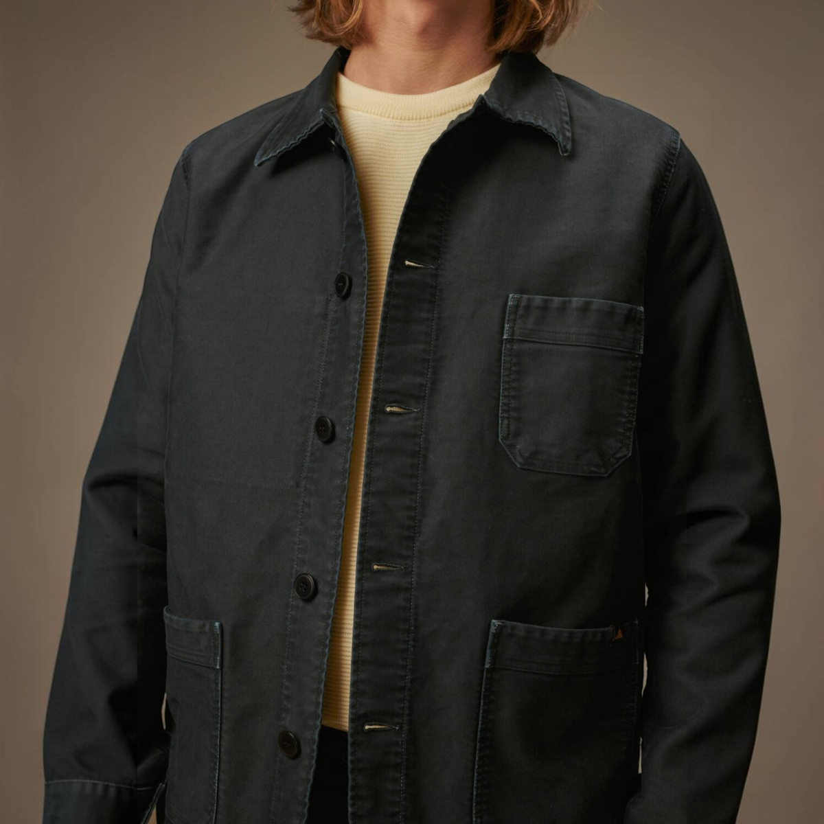MILWORKS vintage washed black moleskin work jacket with button front and patch pockets worn over a yellow sweater