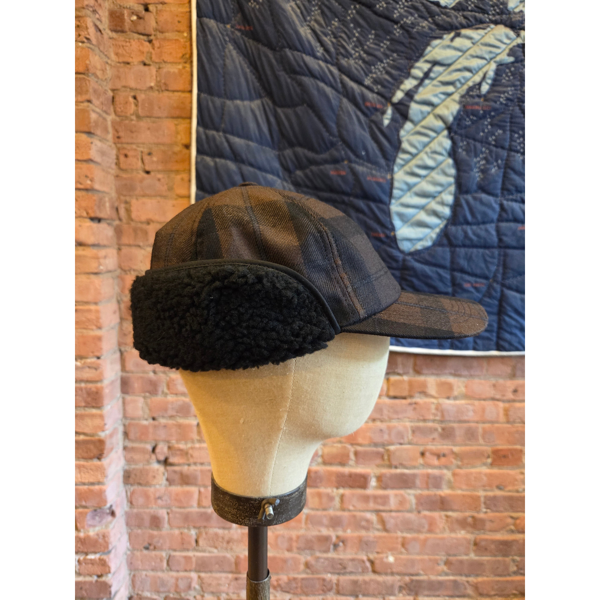 MILWORKS hunting cap in brown and black worsted wool plaid with black fleece ear flaps on a mannequin head