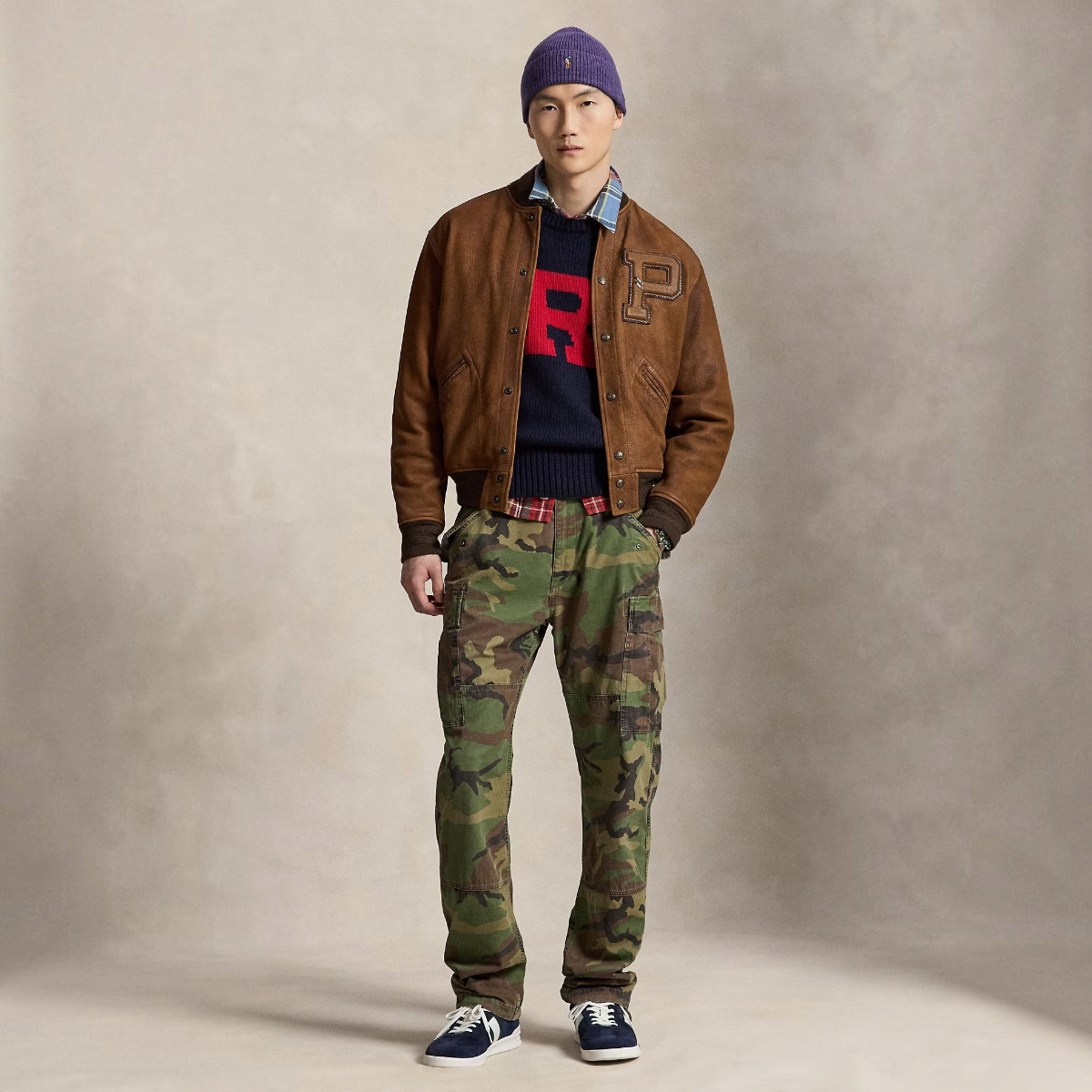 A model wearing MILWORKS camo canvas cargo pants with a brown suede bomber jacket, navy sweater, and purple beanie.