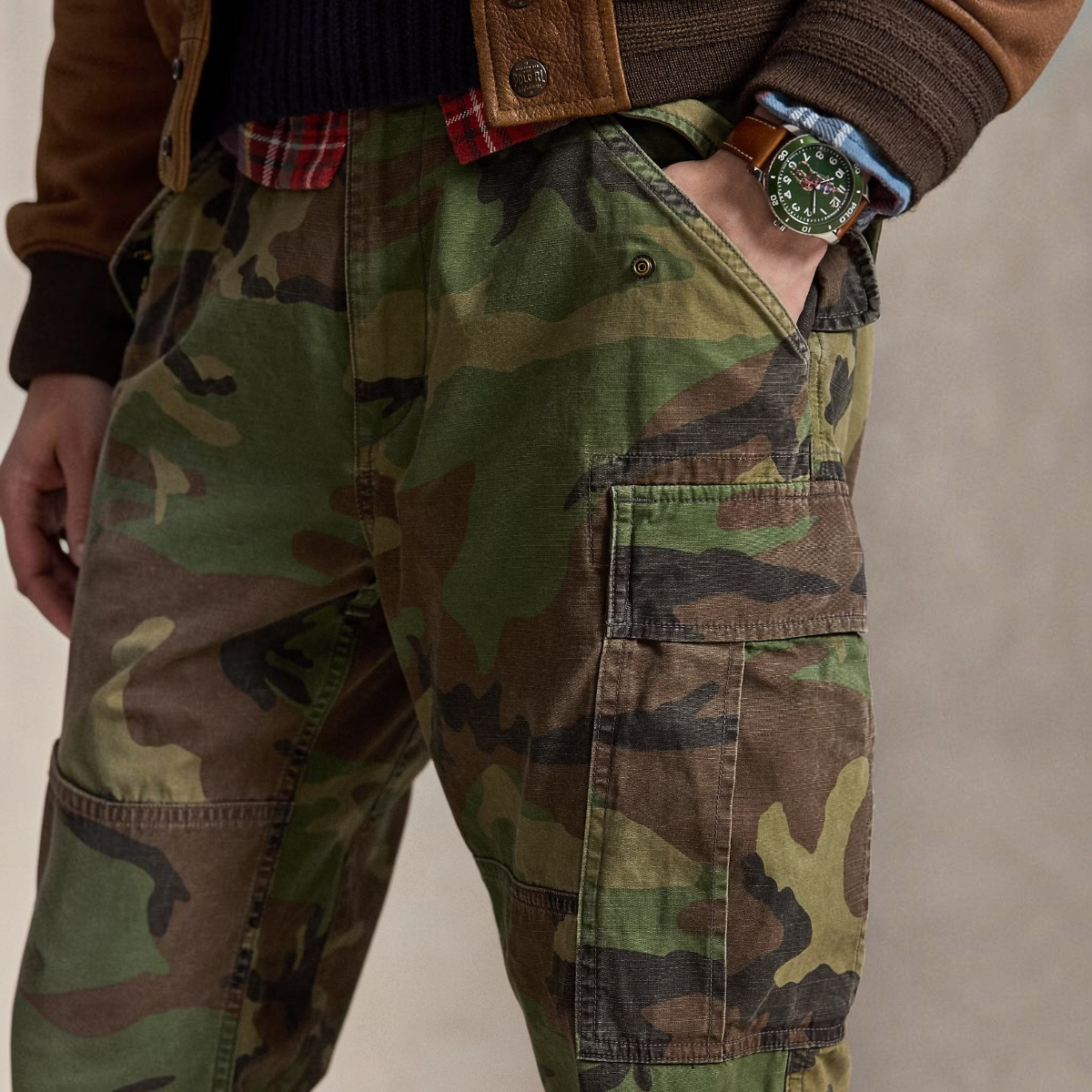 MILWORKS camo canvas cargo pants with side pockets and adjustable waist tabs worn by a model in a brown jacket