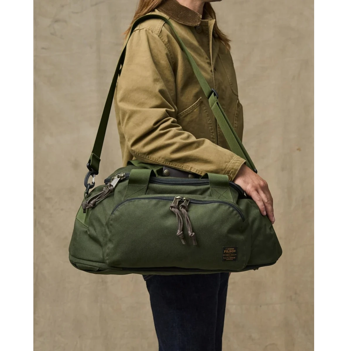 MILWORKS Dryden Duffle Pack in Otter Green nylon with shoulder strap, worn by a person in a green jacket.