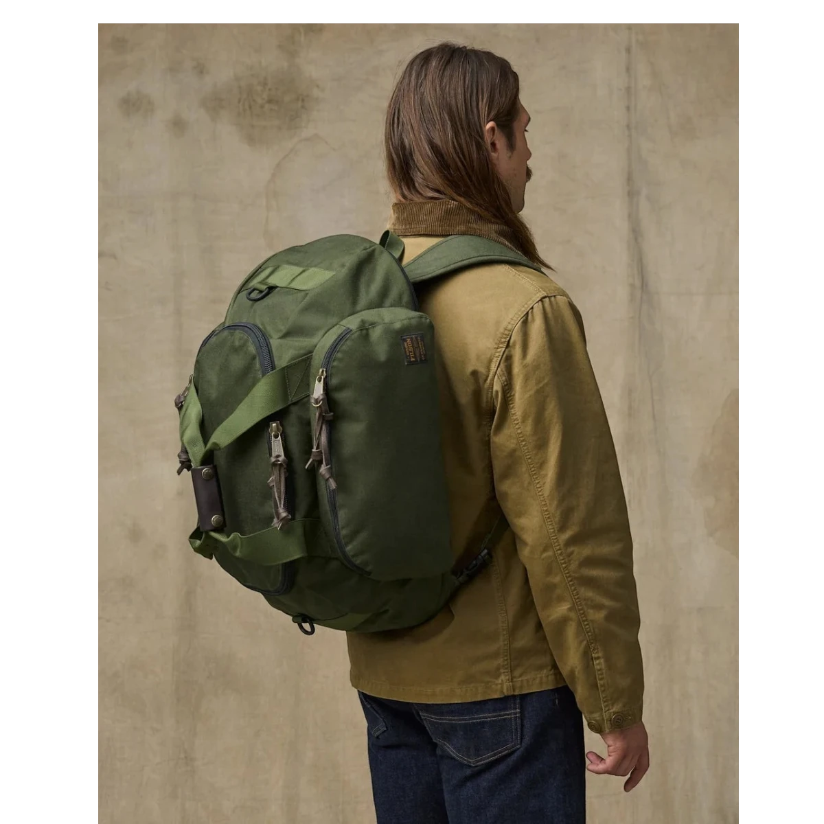MILWORKS Dryden Duffle Pack in otter green 1000D nylon worn as a backpack by a man in a tan jacket