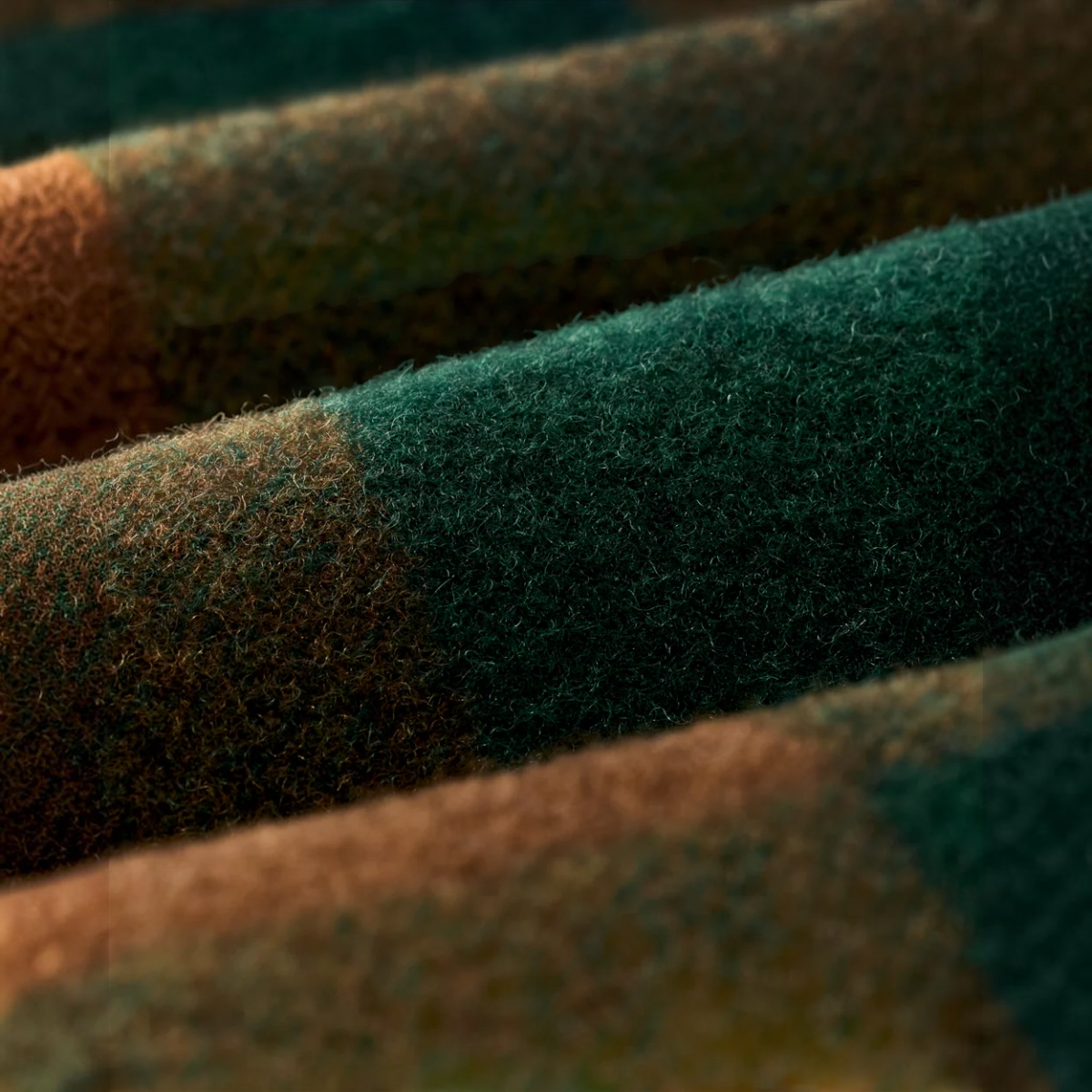 Close-up of MILWORKS Filson wool jac-shirt fabric in bronze green plaid showing the textured weave