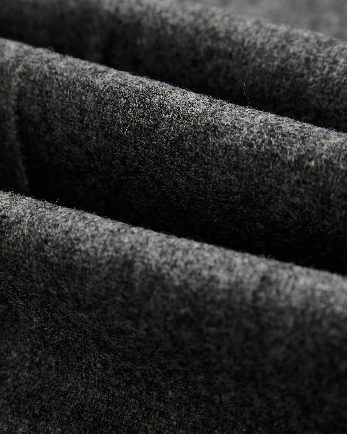 Close-up of grey virgin wool fabric texture showing the pleat detail on MILWORKS single pleat trousers.