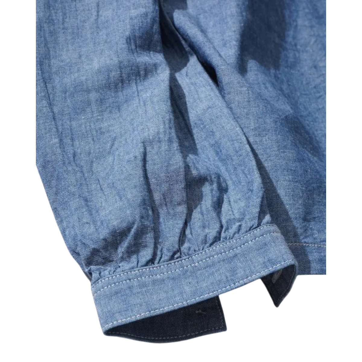 Close-up of the sleeve cuff on a MILWORKS indigo chambray cotton work shirt with visible stitching detail.