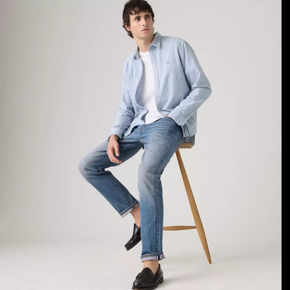 MILWORKS model wearing Levi's 502 Taper medium wash selvedge jeans with a light blue striped shirt and loafers.