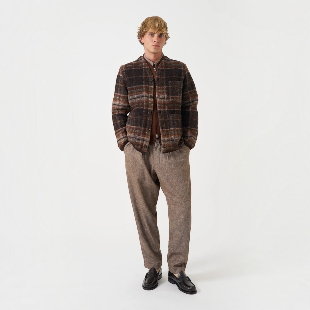 Model wearing a MILWORKS Pino wool fleece cardigan in brown plaid with patch pockets over a brown shirt and trousers.