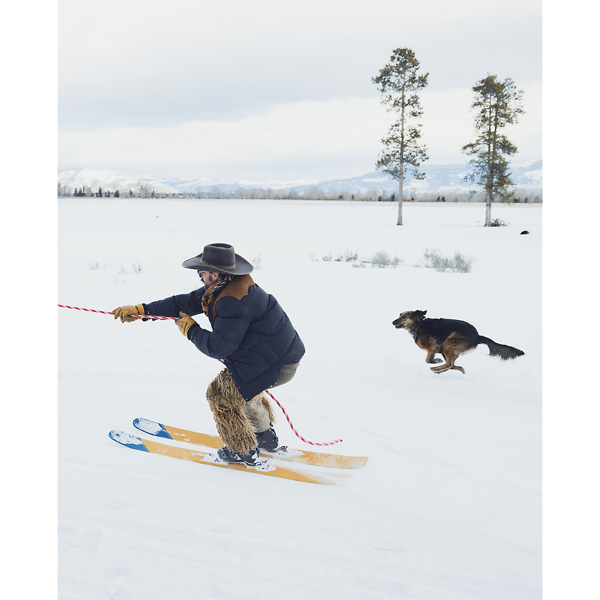 MILWORKS RRL black nylon coat with cowhide and shearling details worn by a skier in a snowy landscape with a dog