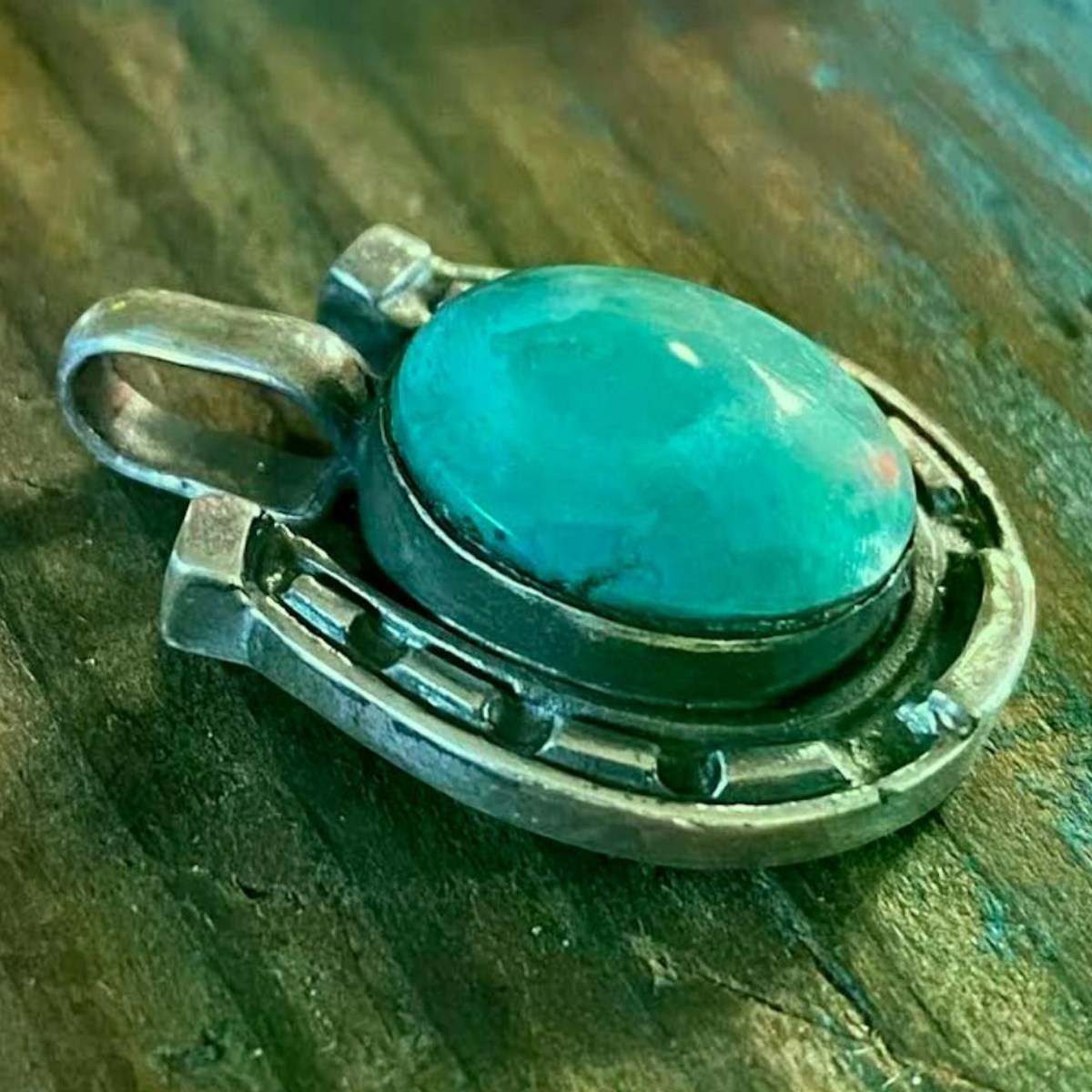 MILWORKS sterling silver horseshoe charm featuring a central oval turquoise stone on a rustic wooden surface.