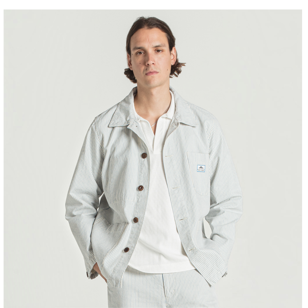 MILWORKS Vins striped cotton work jacket with corozo buttons and two front pockets worn by a man in a studio