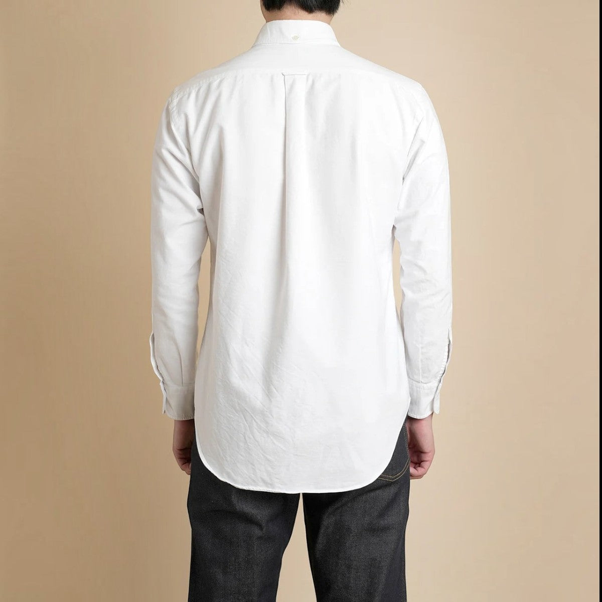 Back view of a MILWORKS white cotton oxford button-down shirt featuring a box pleat and locker loop on a model.