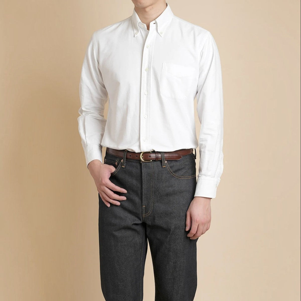 Model wearing a white MILWORKS Vintage Ivy cotton oxford button-down shirt with a chest pocket and shell buttons.